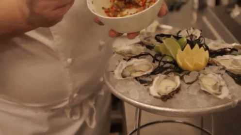 A Person Is Holding A Bowl Of Food Over A Plate Of Oysters And Ice GIF