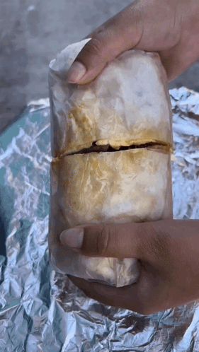 A Person Is Holding A Burrito Wrapped In Foil GIF