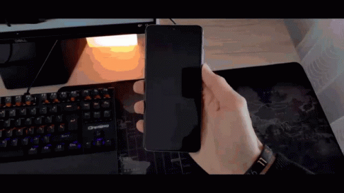 A Person Is Holding A Cell Phone In Front Of A Computer Keyboard GIF