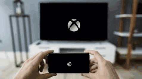 A Person Is Holding A Cell Phone In Front Of An Xbox Logo On A Television . GIF