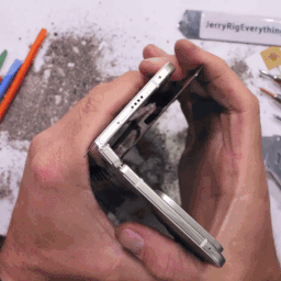 A Person Is Holding A Cell Phone In Their Hands With Jerry Rig Everything Written On A Tube In The Background GIF