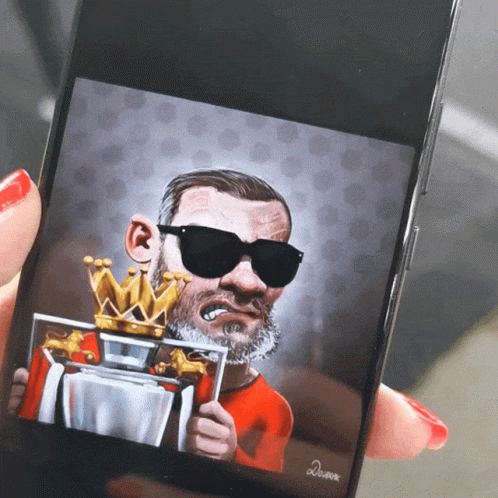 A Person Is Holding A Cell Phone With A Caricature Of A Man Wearing Sunglasses And A Crown GIF