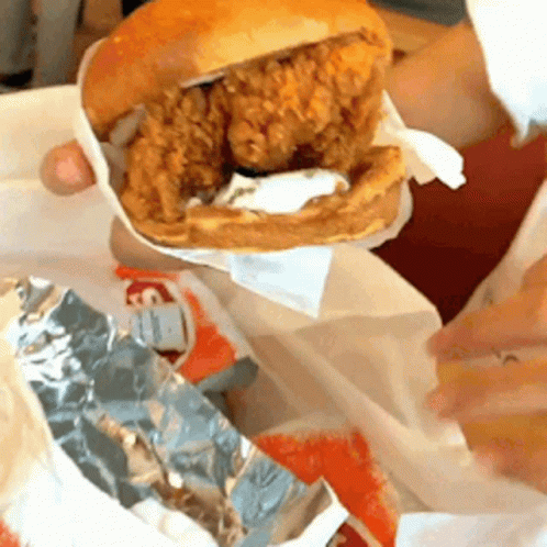 A Person Is Holding A Chicken Sandwich On A Bun GIF