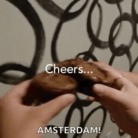A Person Is Holding A Chocolate Donut In Their Hands With The Words `` Cheers Amsterdam '' Written On It . GIF
