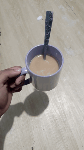 a person is holding a cup of coffee with a spoon sticking out of it