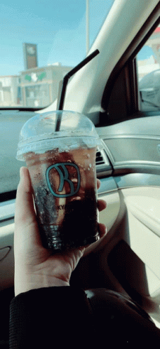 A Person Is Holding A Cup Of Coffee With A Straw In A Car GIF