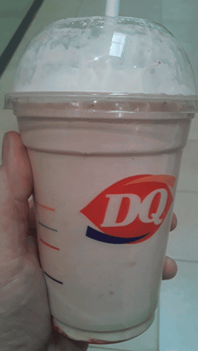 A Person Is Holding A Cup Of Dq Milkshake In Their Hand GIF