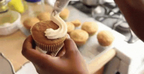 a person is holding a cupcake with frosting on it in their hand .