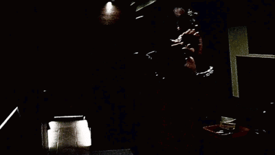 A Person Is Holding A Fan In Front Of A Couch In A Dark Room . GIF