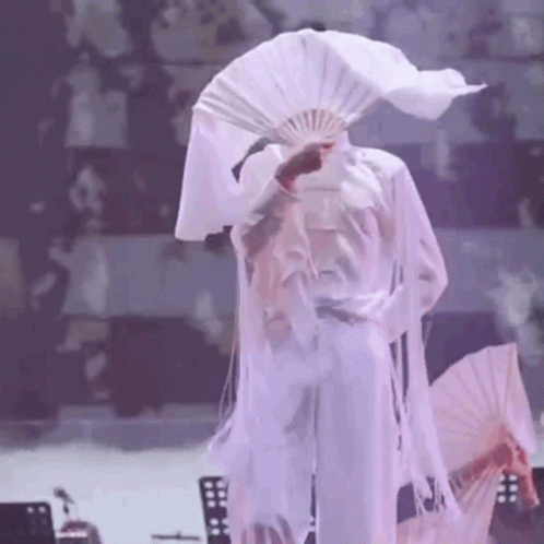 A Person Is Holding A Fan In Front Of Their Face . GIF