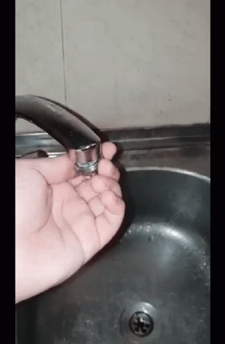 A Person Is Holding A Faucet In Their Hand In Front Of A Sink GIF