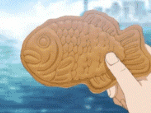 A Person Is Holding A Fish Shaped Biscuit In Their Hand . GIF