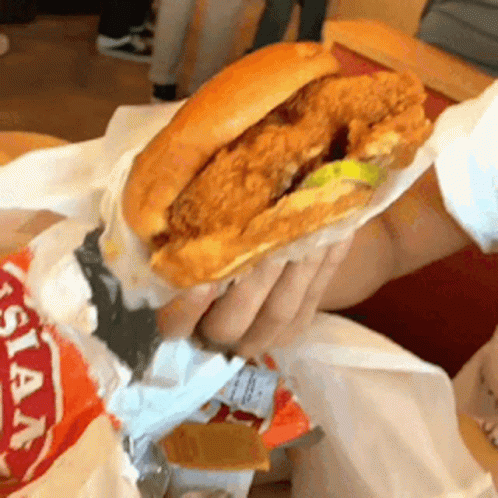 A Person Is Holding A Fried Chicken Sandwich In Their Hand .. GIF