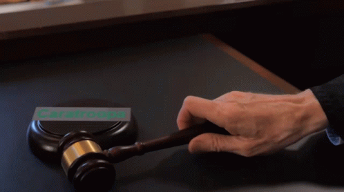 A Person Is Holding A Gavel In Front Of A Sign That Says Caratroops GIF