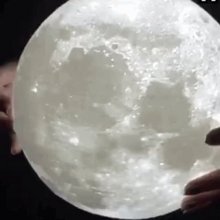 A Person Is Holding A Giant Moon In Their Hands . GIF