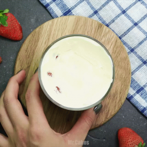 A Person Is Holding A Glass Of Milk On A Wooden Cutting Board With The Words Mr. Cakes Written On The Bottom GIF