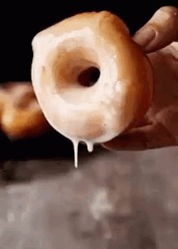 A Person Is Holding A Glazed Donut In Their Hand With Icing Dripping Out Of It . GIF