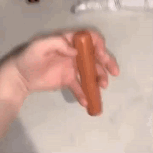 A Person Is Holding A Hot Dog In Their Hand On A Counter . GIF
