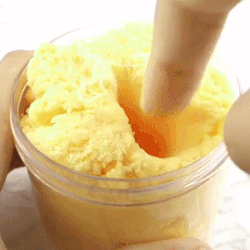 A Person Is Holding A Jar Of Yellow Slime With A Spoon . GIF