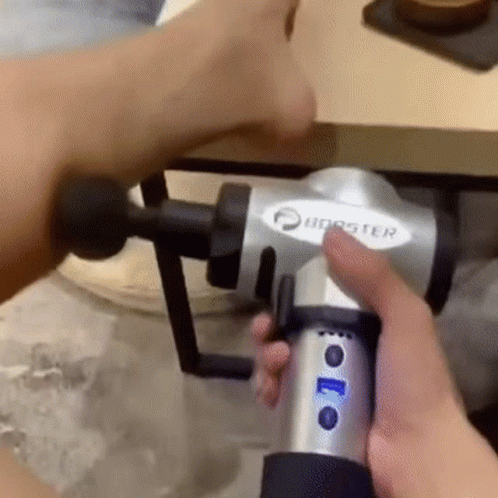 A Person Is Holding A Massage Gun In Their Hand And Using It On Their Arm . GIF