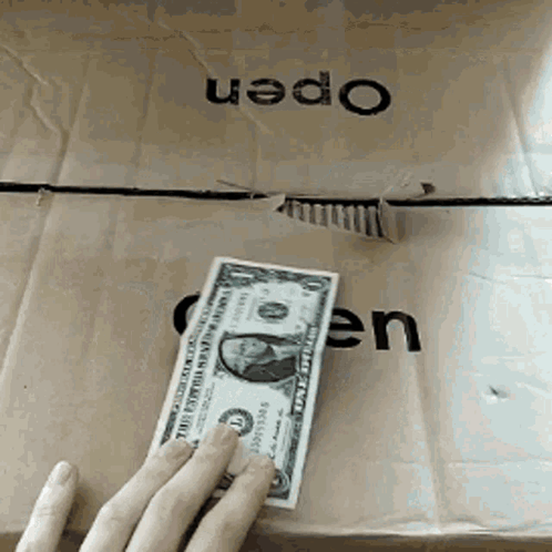 A Person Is Holding A One Dollar Bill In Front Of A Cardboard Box That Says Open GIF