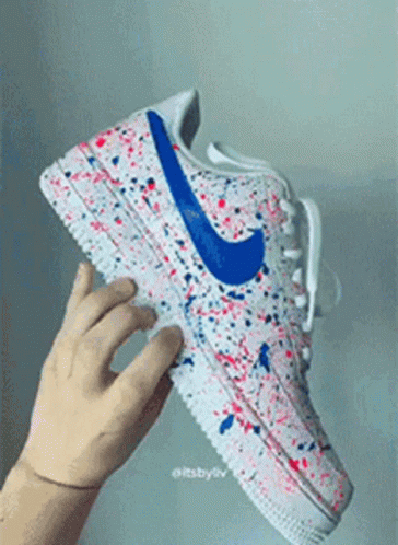 A Person Is Holding A Pair Of Nike Air Force 1 Sneakers With Red , White And Blue Paint Splatter On Them . GIF