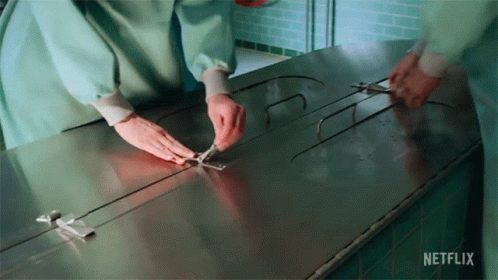 A Person Is Holding A Pair Of Scissors Over A Stainless Steel Table That Says Netflix On It . GIF