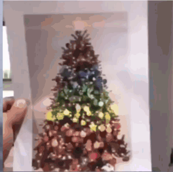 A Person Is Holding A Picture Of A Christmas Tree On A Piece Of Paper GIF