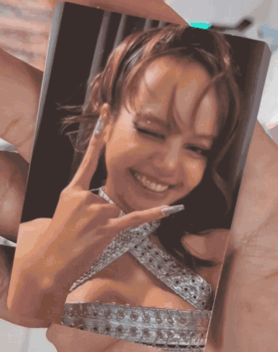A Person Is Holding A Picture Of A Woman In A Silver Dress Making A Peace Sign GIF