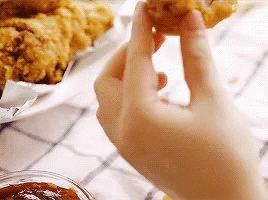 A Person Is Holding A Piece Of Fried Chicken . GIF