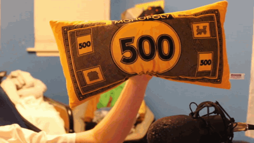 A Person Is Holding A Pillow That Looks Like A Monopoly Money GIF