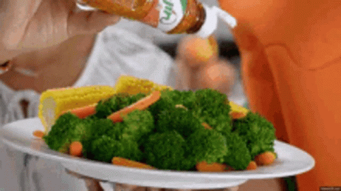 A Person Is Holding A Plate Of Broccoli Carrots And Corn GIF