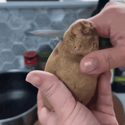 A Person Is Holding A Potato In Their Hands With A Knife In It GIF