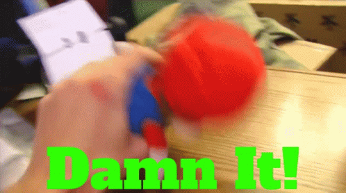 A Person Is Holding A Red Ball With The Words Damn It Written In Green GIF