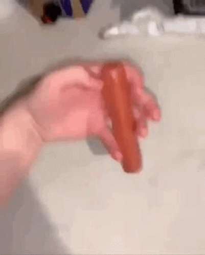 A Person Is Holding A Red Hot Dog In Their Hand . GIF