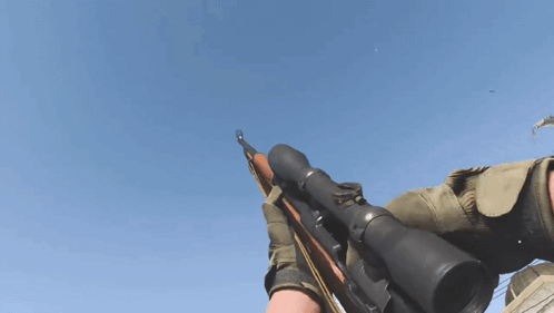A Person Is Holding A Rifle With A Scope On It Against A Blue Sky GIF