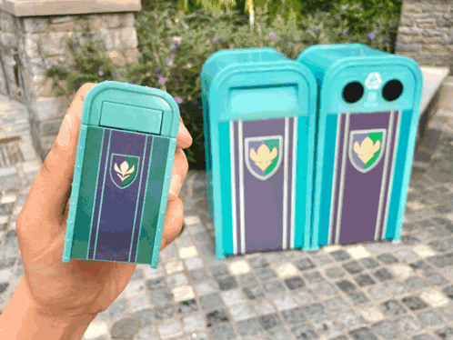 A Person Is Holding A Small Blue Trash Can With A Shield On It GIF