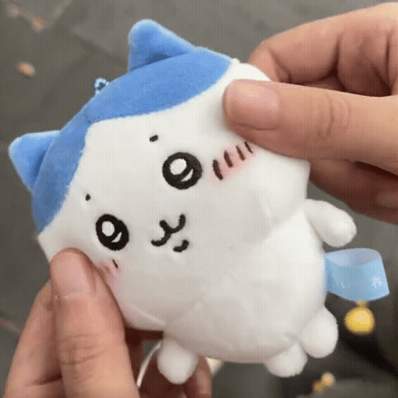A Person Is Holding A Stuffed Animal With A Blue And White Cat On It 'S Face . GIF