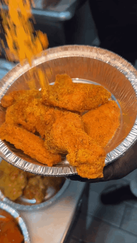 A Person Is Holding A Tin Foil Container Of Chicken Wings GIF