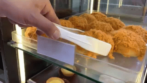 A Person Is Holding A Tong Over A Display Case Of Food GIF