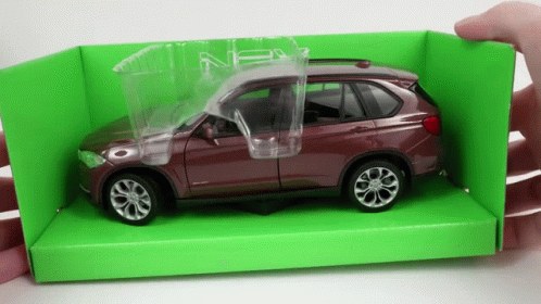 A Person Is Holding A Toy Car In A Green Box With The Door Open GIF