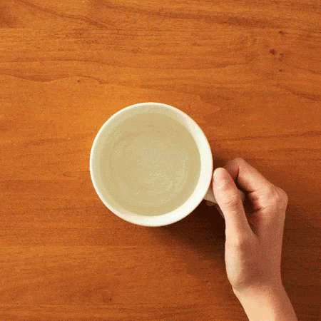 a person is holding a white cup of water on a wooden table