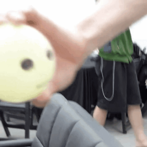 A Person Is Holding A Yellow Ball In Their Hand With A Smiley Face On It . GIF