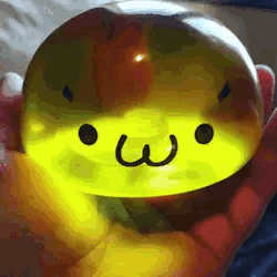 A Person Is Holding A Yellow Sphere With A Face On It . GIF