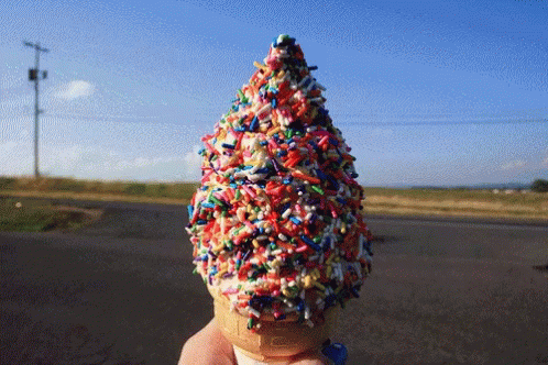 A Person Is Holding An Ice Cream Cone With Sprinkles On It GIF