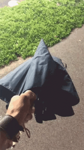 A Person Is Holding An Umbrella In Their Hand On A Sidewalk GIF