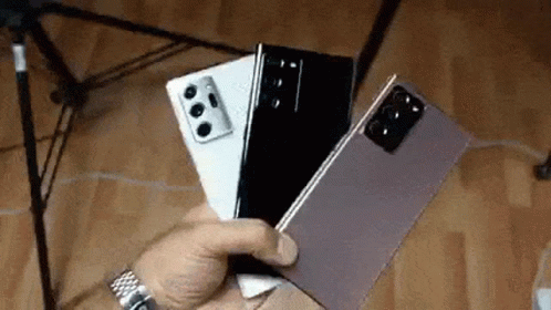 A Person Is Holding Three Cell Phones In Their Hand . GIF