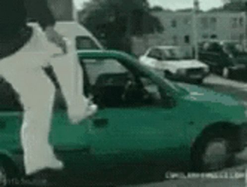 A Person Is Jumping Out Of A Green Car On A Street GIF