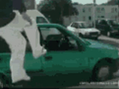 A Person Is Jumping Out Of A Green Car With A White Shirt On . GIF
