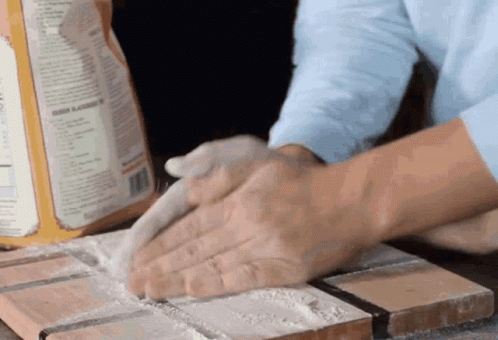 A Person Is Kneading A Dough On A Cutting Board With A Box Of Flour In The Background GIF